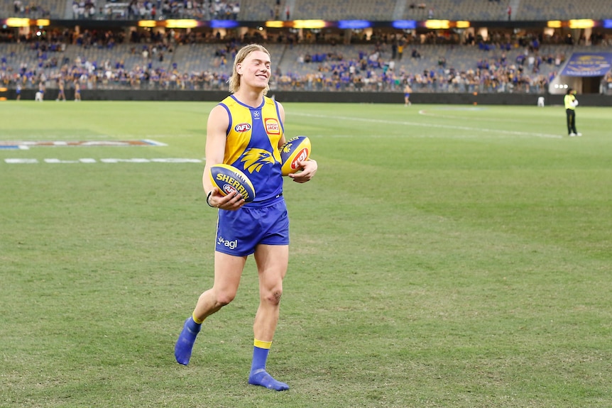 West Coast Eagles player Harley Reid smiles while carrying two footballs after a match.